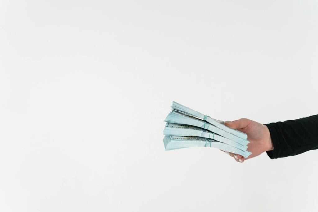 Close-up of a hand holding bundles of American dollar bills against a white background.